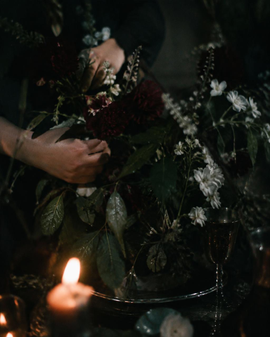 Hands arranging dark stems beside a candle and a silver goblet